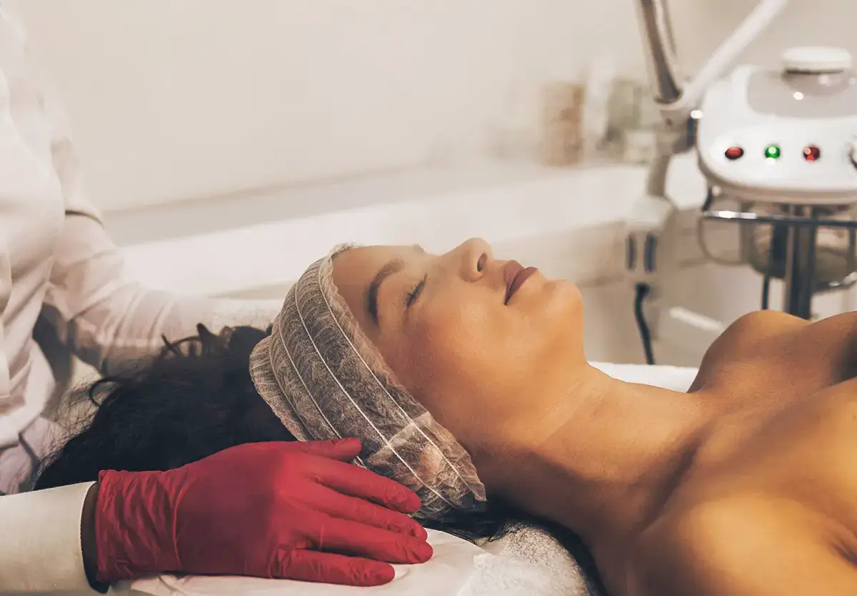 Salon De Înfrumusețare Baia Mare - O femeie stând confortabil cu un vapozon aplicat pe față, în timp ce beneficiază de un tratament facial revitalizant într-un salon de înfrumusețare.